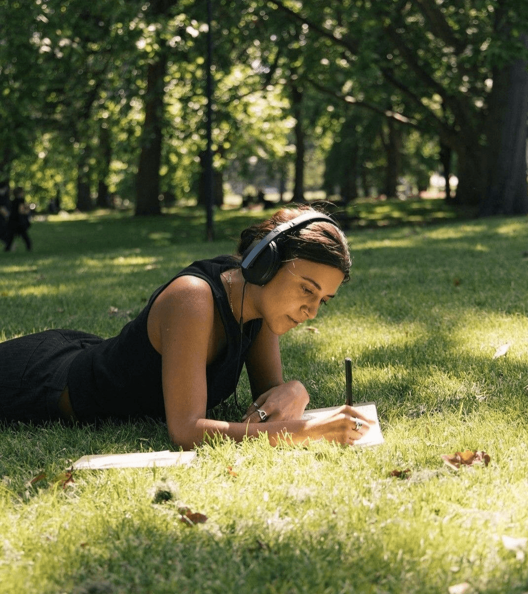 Person relaxing outdoors with headphones, writing in a notebook on the grass
